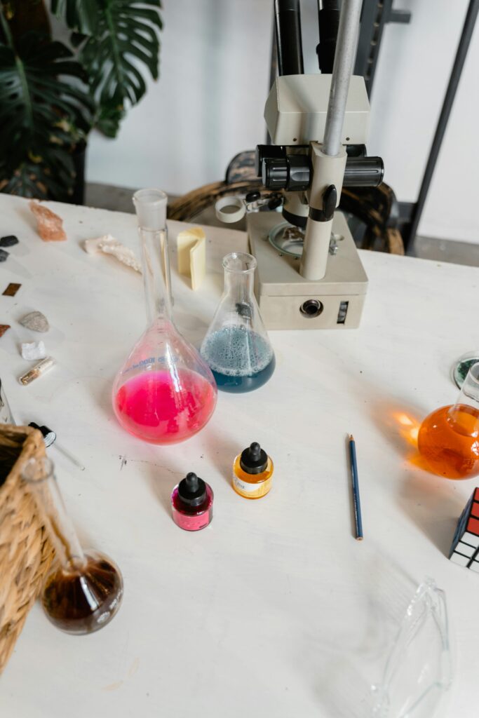 A laboratory setup featuring flasks with colored liquids and a microscope on a white table.